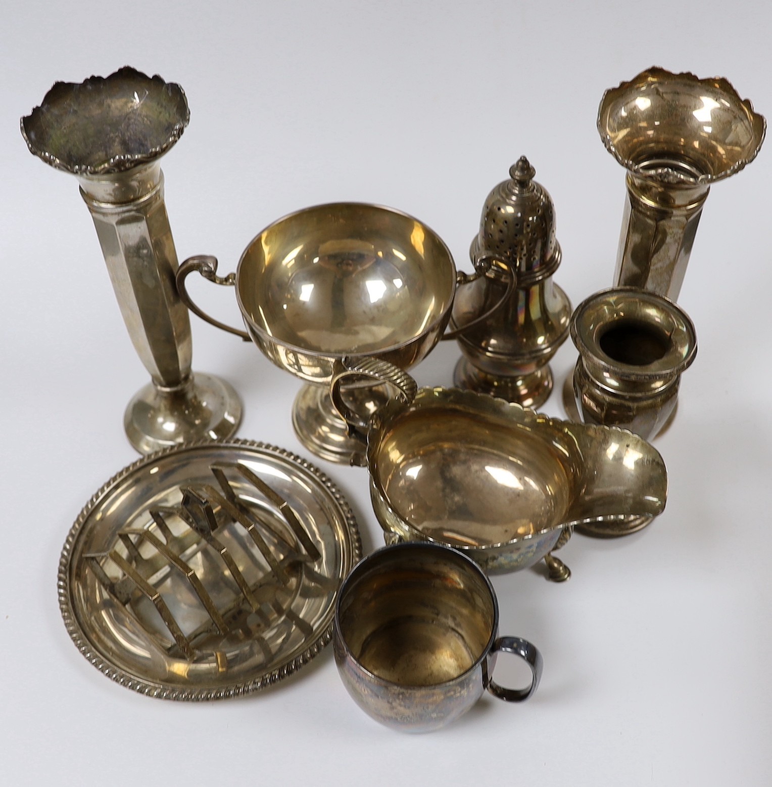 Assorted silver ware including a pair of George V spill vases, a small vase, a two handled trophy cup, sauceboat, mug, caster, stand and toastrack.